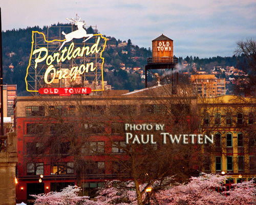 The iconic "Portland,  Oregon" sign from the Burnside Bridge in spring. The sign has gone through several evolutions,  but has always had the map of Oregon. The "White Stag" clothing company added the deer and the city of Portland added the current text. Every spring,  flowering cherry trees festoon Waterfront Park below the sign. An old wooden water tower bearing the moniker "Old Town" occupies the rooftop next to the sign.